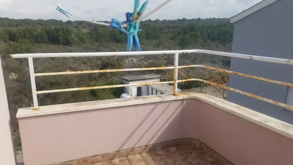 Rusty balcony railing with visible corrosion in an outdoor setting, needing maintenance.