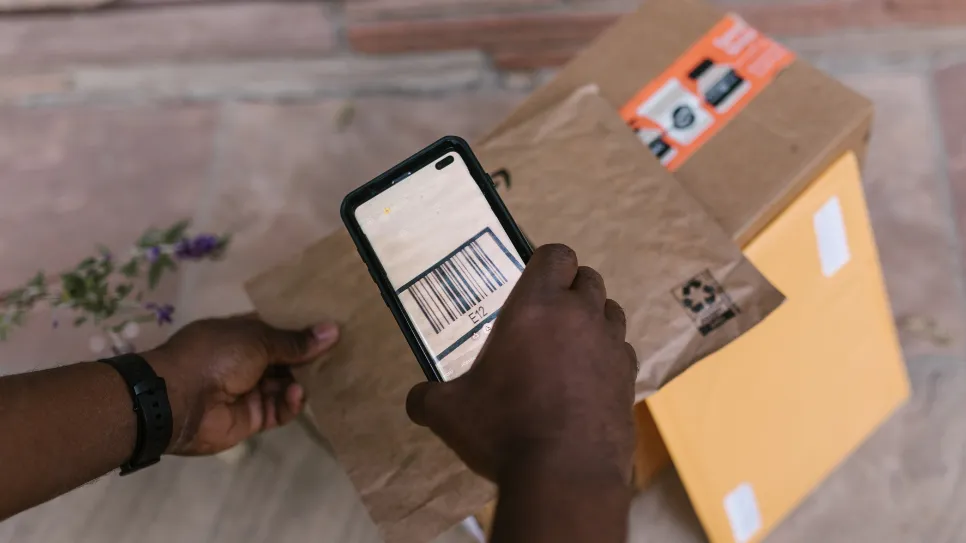 A person uses a smartphone to scan the barcode on a package, with other parcels ready for shipping or return in the background.